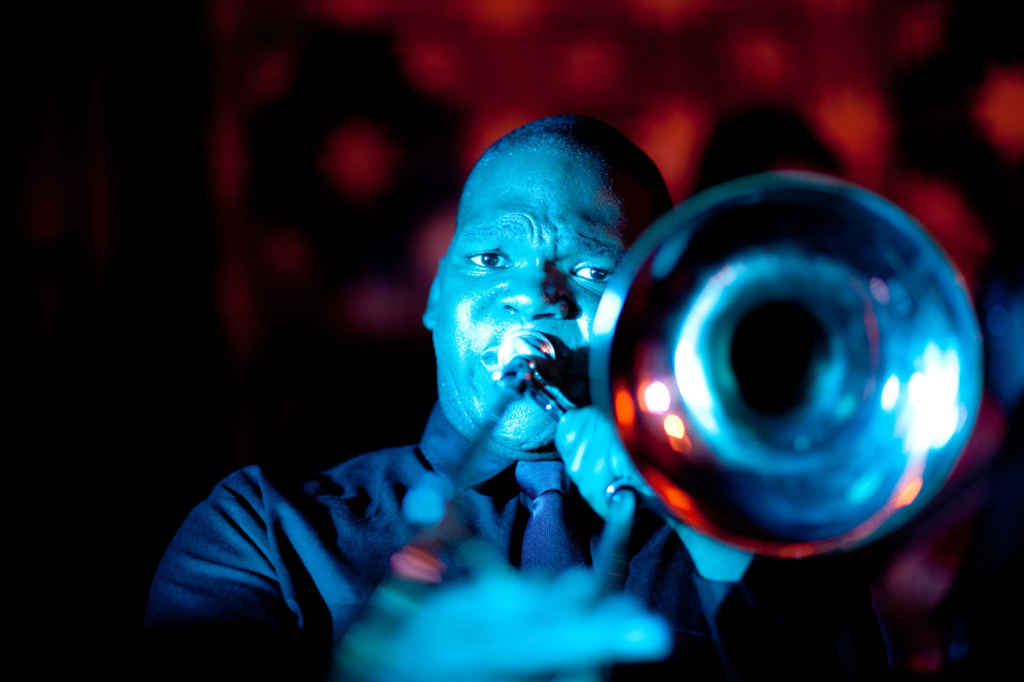 Blue-lit trombone player performing passionately on stage with vibrant red and blue lighting.