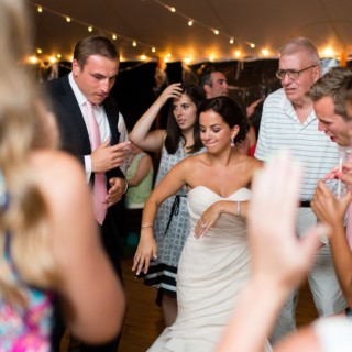 Bride dancing joyfully with guests under glowing tent lights at Newagen Seaside Inn wedding.