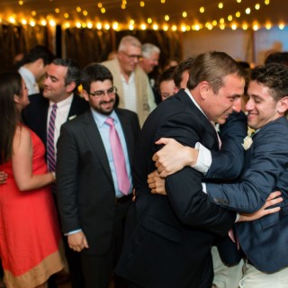 Two men share a joyful embrace at a lively Newagen Seaside Inn wedding in Maine.