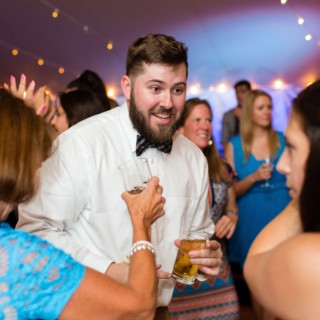 Bearded man laughing with guests under warm string lights at Newagen Seaside Inn wedding reception.