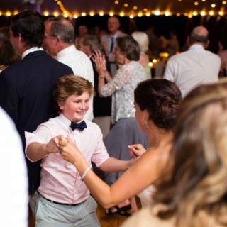 Woman and young boy dancing joyfully under warm string lights at a coastal Maine wedding.