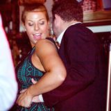 Smiling couple dancing closely under warm lights at a lively wedding celebration.
