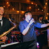 Live band performing at rustic barn wedding with warm lights and energetic musicians.