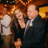 Father and daughter laughing while dancing at a warm, rustic barn wedding celebration in New York.