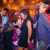 Energetic live band performing at rustic barn wedding with warm string lights and vibrant atmosphere.