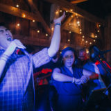 Energetic live band performing at rustic barn wedding with passionate singers and warm string lights.