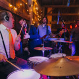 Energetic wedding band performing live in rustic barn under warm string lights.