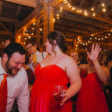 Guests dancing and celebrating under warm string lights at a rustic barn wedding in New York.
