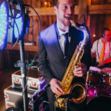 Jazz saxophonist performing live at a rustic barn wedding with warm lights and vibrant atmosphere.