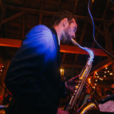 Jazz saxophonist performing live at rustic barn wedding with warm lights and lively atmosphere.