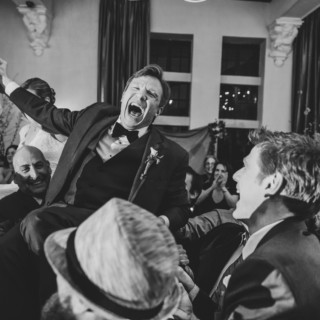 Joyful groom lifted on chair during lively Alden Castle wedding celebration in Brookline, Massachusetts.