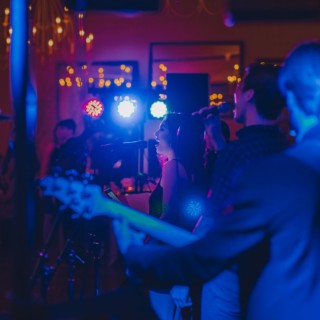 Live band performing under colorful stage lights at an intimate indoor wedding celebration.