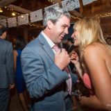 Smiling couple dancing joyfully at rustic Vermont wedding reception under warm string lights.