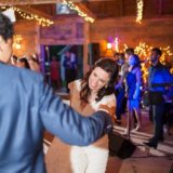 Bride and groom dancing joyfully under string lights at rustic barn wedding in Bristol, Vermont.