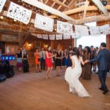 Bride and groom dancing joyfully in a rustic Vermont barn wedding with papel picado and lights.