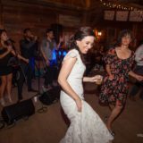 Bride dancing joyfully at rustic Vermont barn wedding with live band and warm string lights.