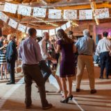 Guests dancing at a rustic barn wedding reception with warm lights and festive papel picado décor.