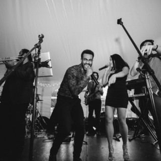 Black and white photo of an energetic live wedding band performing under a tent.