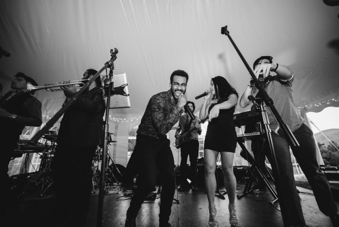 Black and white photo of an energetic live wedding band performing under a tent.
