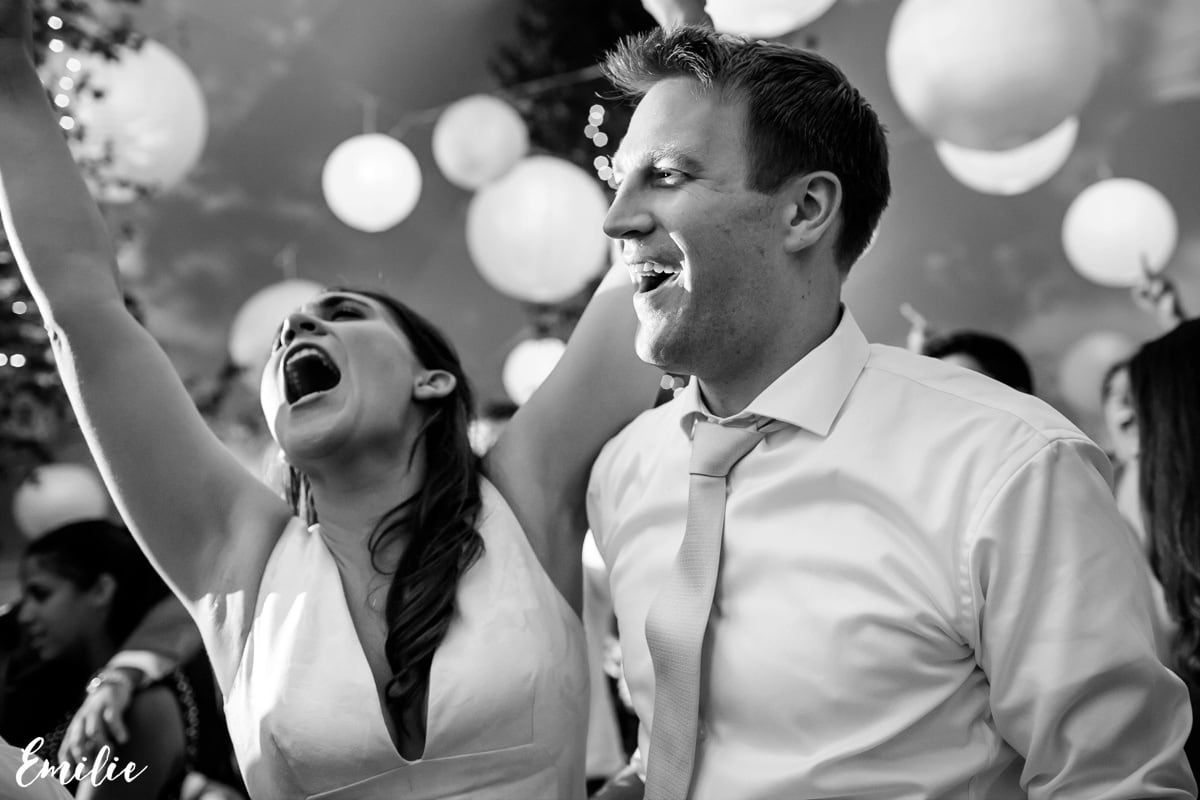 Joyful couple dancing under string lights at a black-and-white wedding celebration in Bar Harbor.