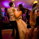 Couple dancing joyfully at elegant Bar Harbor wedding under warm golden and purple lights.