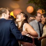 Bride and groom laughing and dancing under warm lantern lights at a joyful wedding reception.