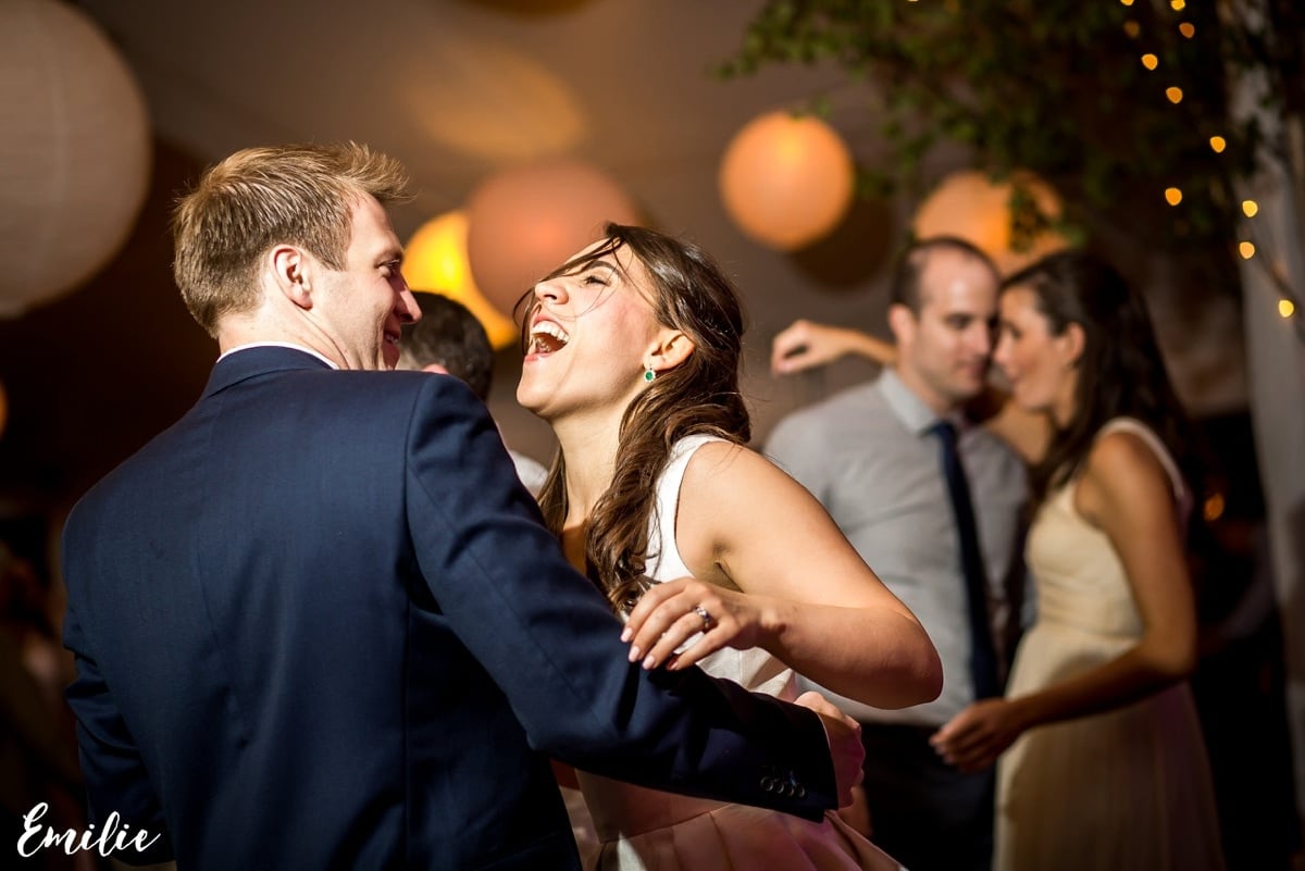 Bride and groom laughing and dancing under warm lantern lights at a joyful wedding reception.