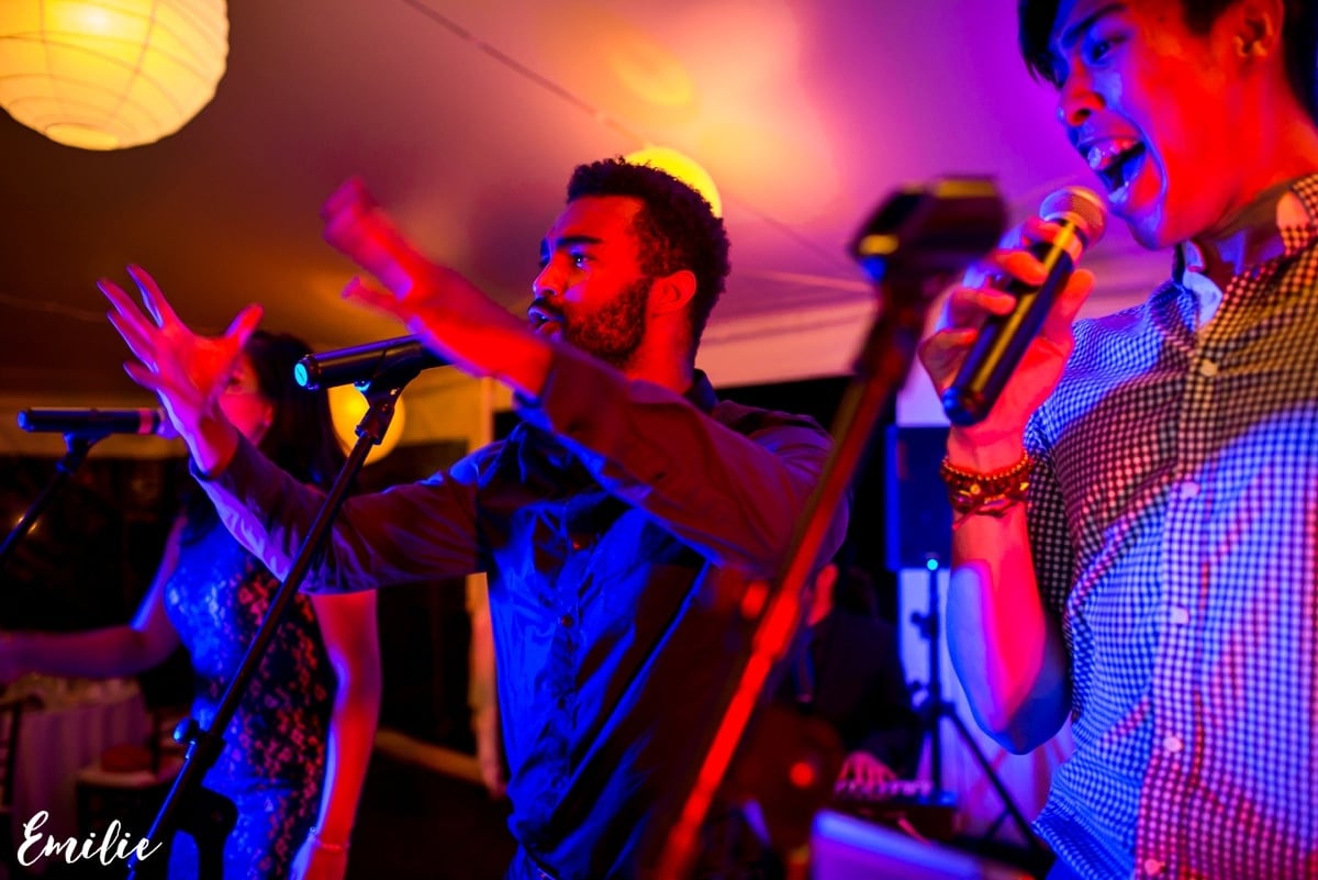 Three singers performing energetically under colorful lights at a lively wedding reception.