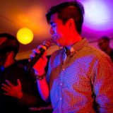 Two male singers performing passionately on stage under vibrant red and purple concert lighting.