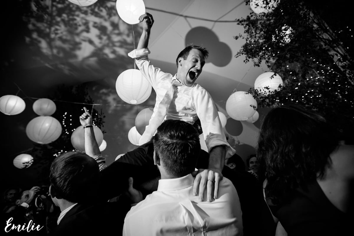 Groom lifted joyfully by friends under glowing lanterns at lively Bar Harbor wedding celebration.