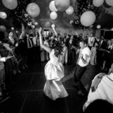 Bride and groom dancing joyfully under lanterns surrounded by cheering guests at elegant wedding reception.