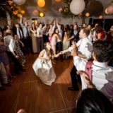 Bride and groom dancing joyfully at Maine wedding reception surrounded by cheering guests and glowing lanterns.