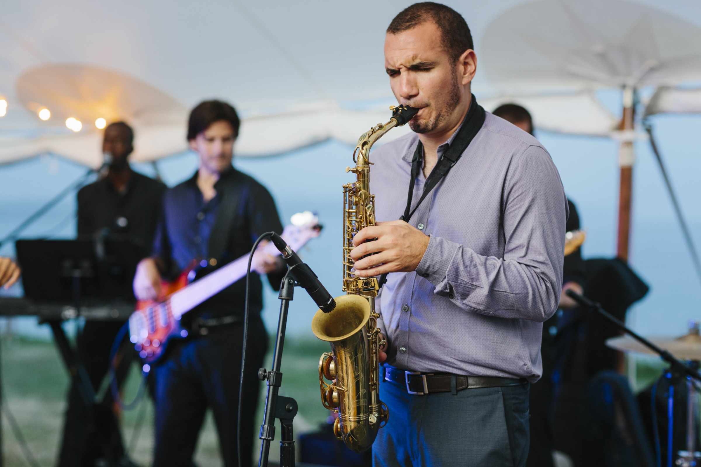 Saxophonist performing live under white canopy at seaside wedding reception on Cuttyhunk Island.