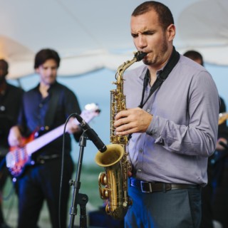 Saxophonist performing live under white canopy at seaside wedding reception on Cuttyhunk Island.