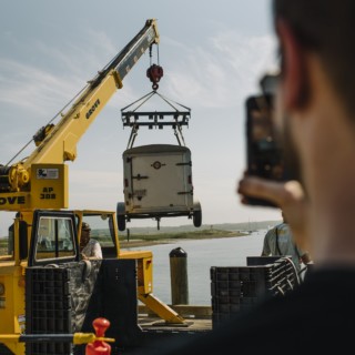 Yellow GROVE crane lifting industrial equipment at waterfront dock under clear blue sky.