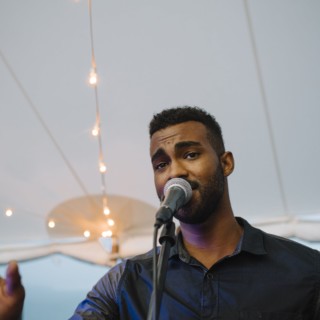 Bearded singer performing under warm string lights at Cuttyhunk Island wedding reception.