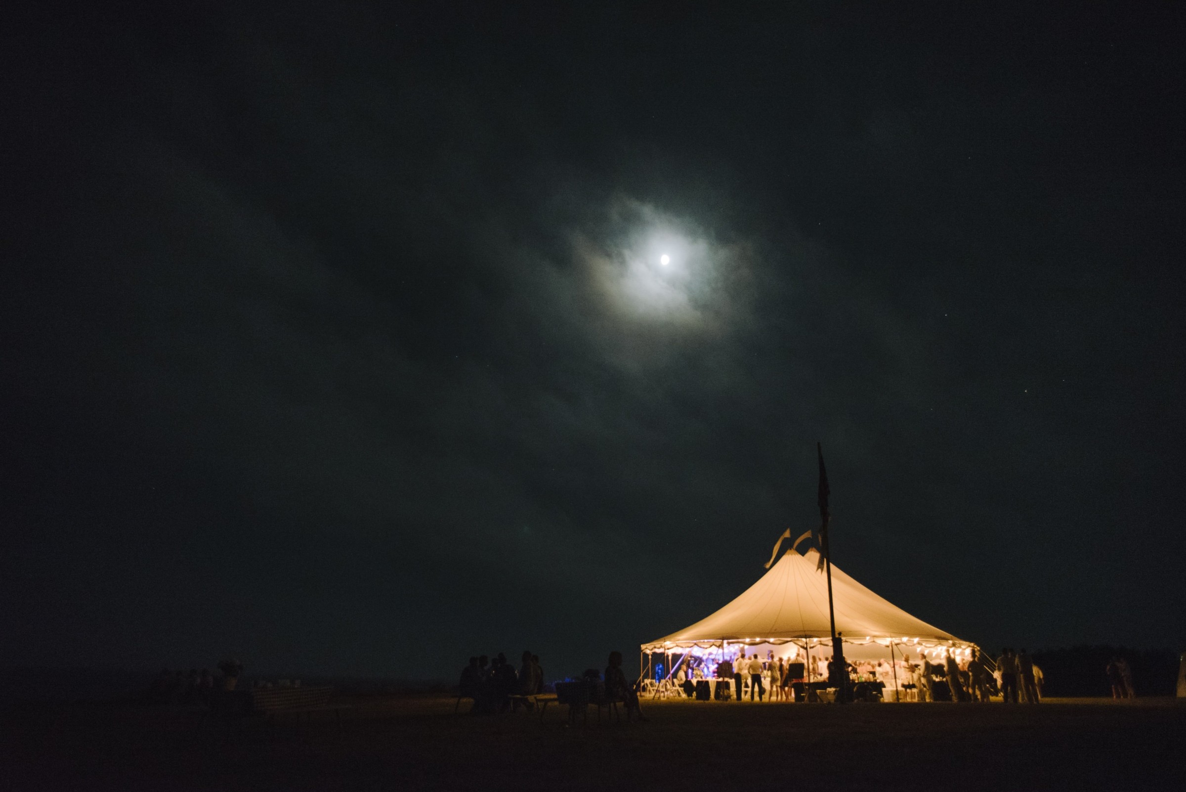Moonlit wedding tent glowing on Cuttyhunk Island under a starry coastal night sky.
