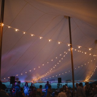 Evening wedding celebration under glowing string lights with live music and dancing guests.
