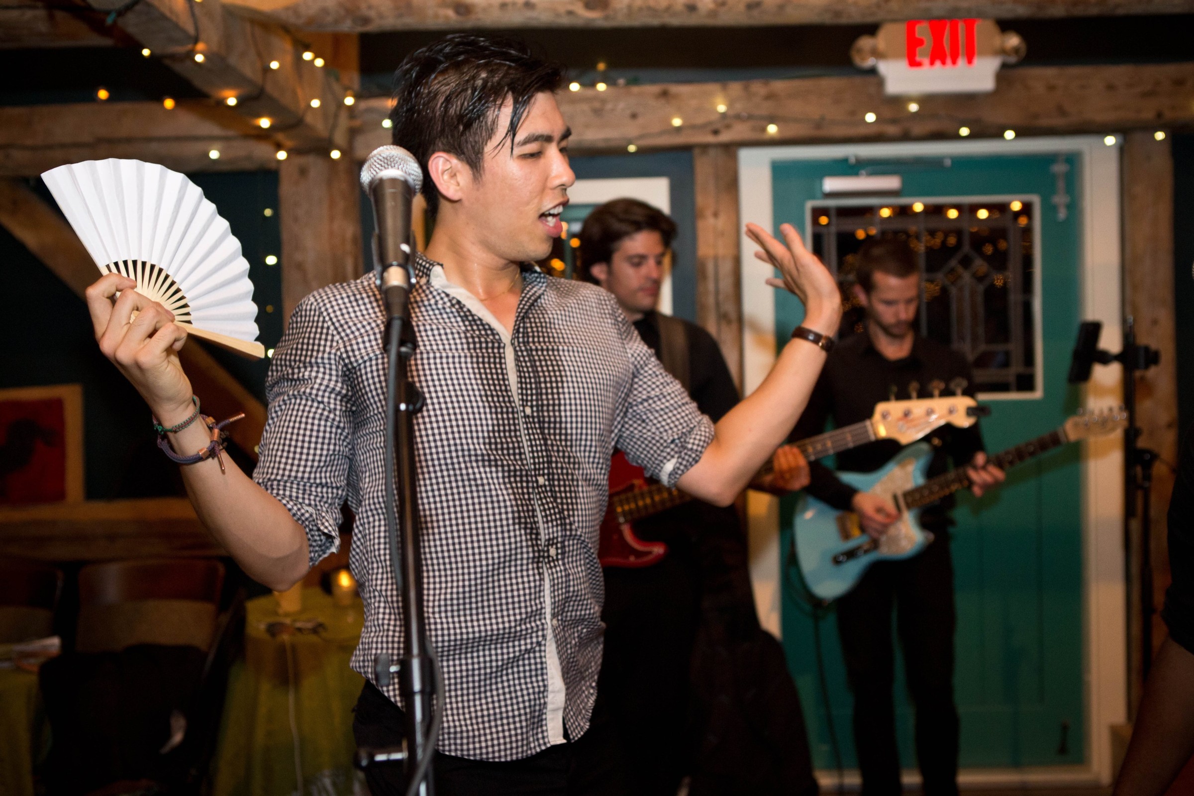 Energetic singer performing with musicians in a cozy, rustic venue illuminated by warm string lights.