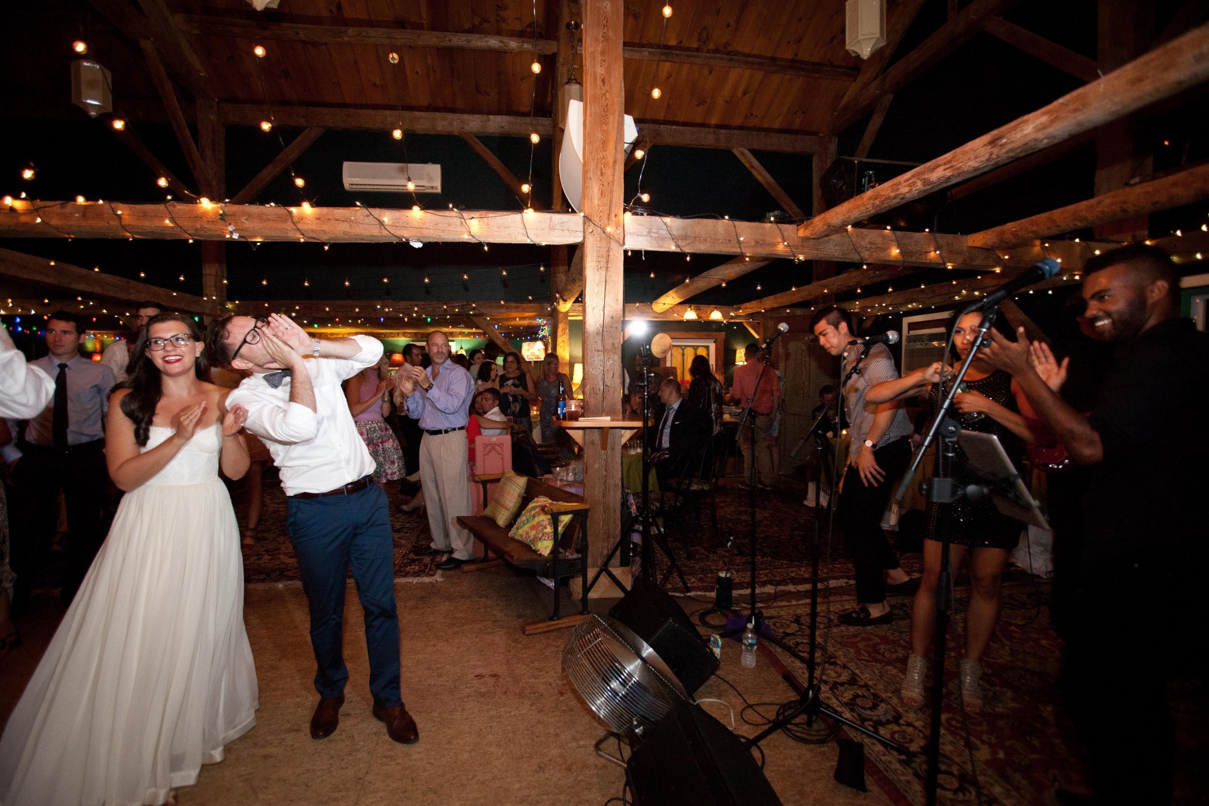 Bride and groom celebrating with guests during a lively barn wedding reception with live music.