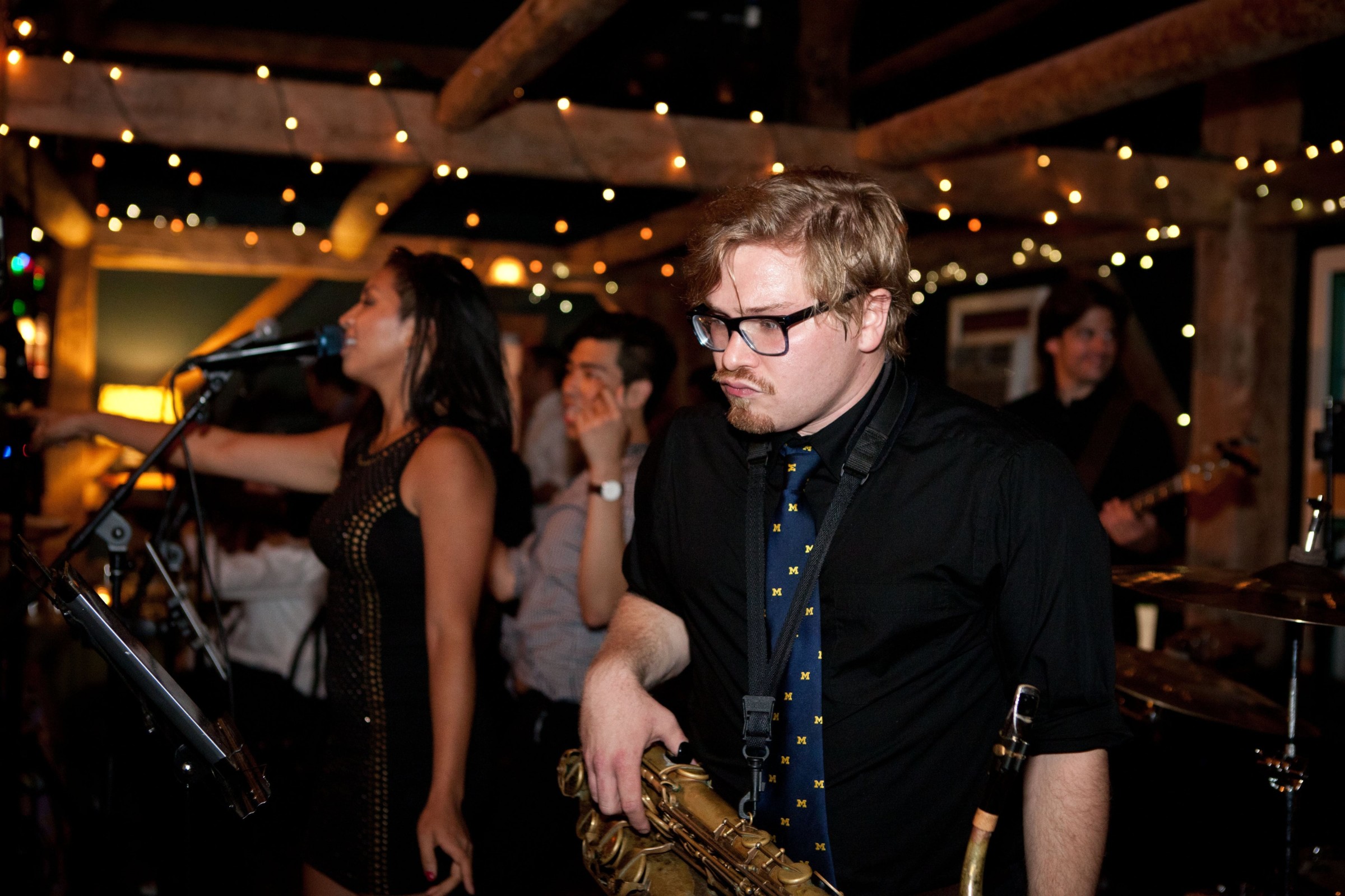 Saxophonist and singer performing live at a rustic music venue with warm ambient lighting.