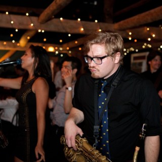 Saxophonist and singer performing live at a rustic music venue with warm ambient lighting.