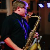Jazz saxophonist performing passionately under warm lights at an intimate live indoor concert.