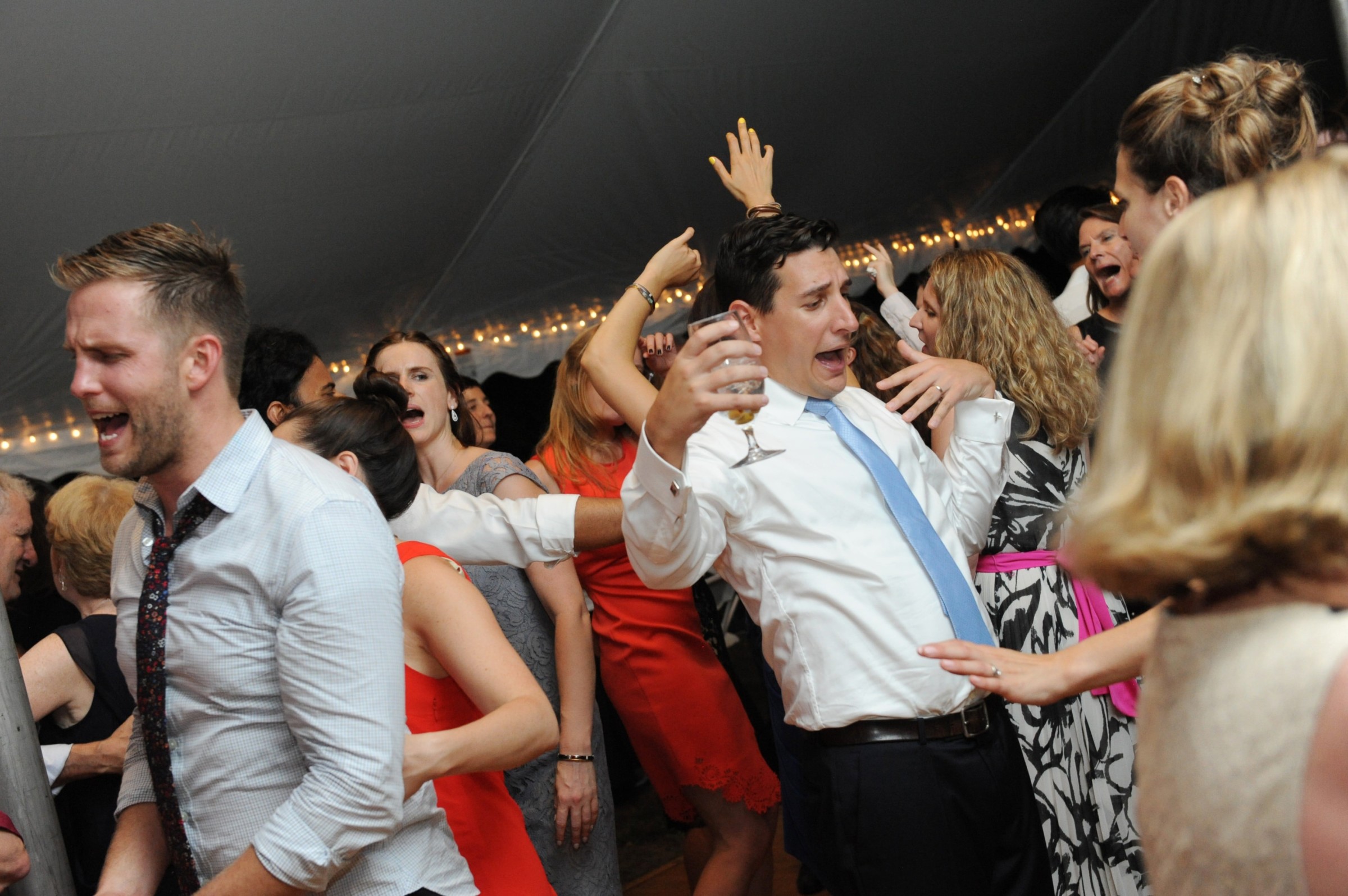 Guests dancing and celebrating under warm string lights at a lively Boston wedding reception.