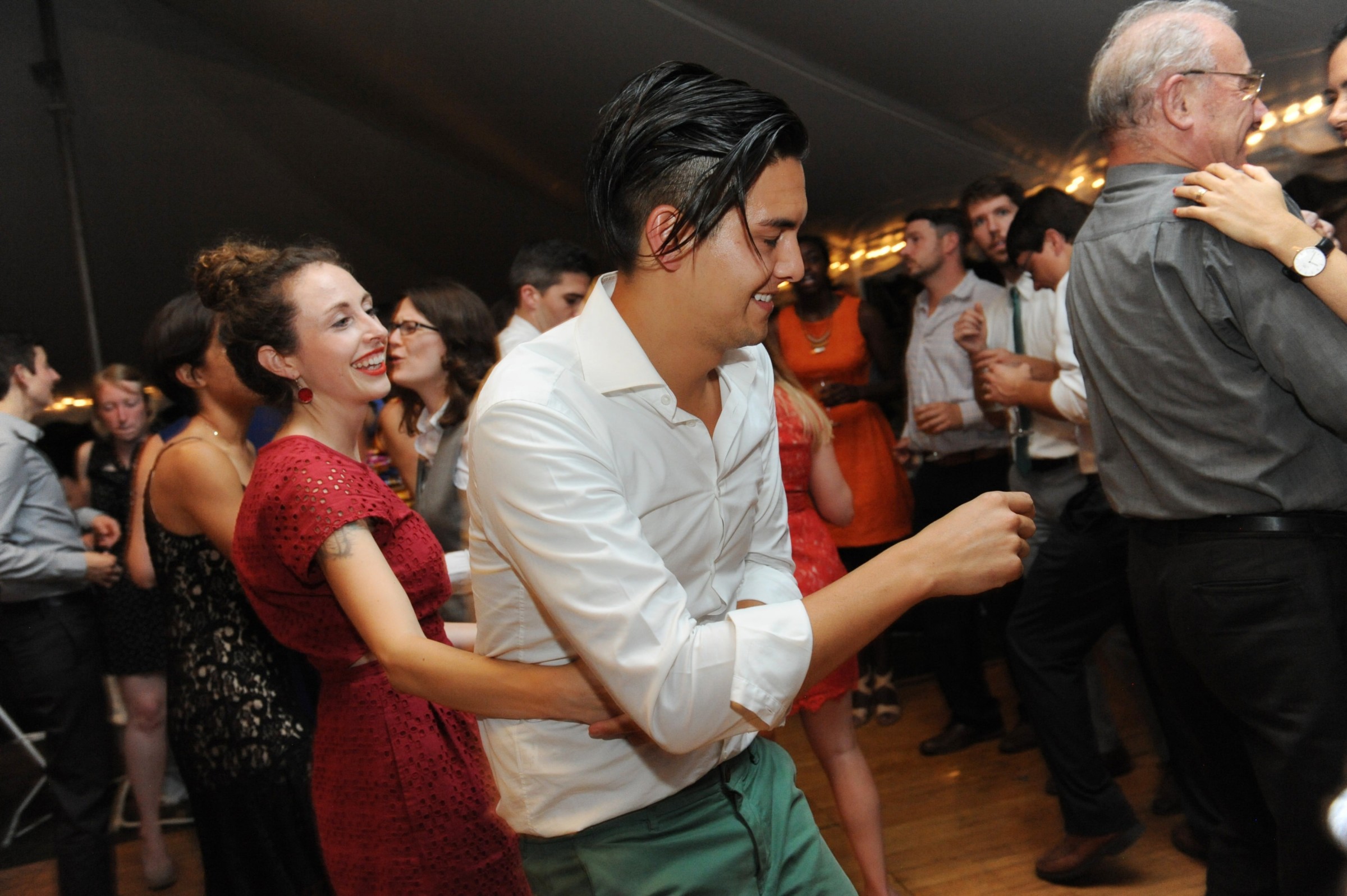 Couple dancing joyfully at Boston wedding reception surrounded by guests under warm golden lights.