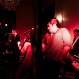Musicians performing passionately under red stage lighting at an elegant indoor wedding venue.