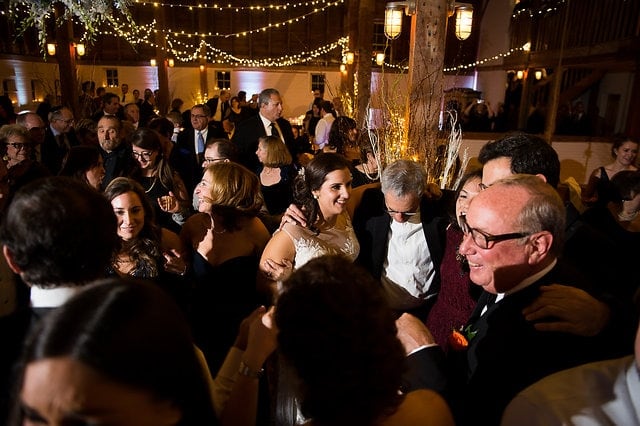 Bride and guests dancing under warm string lights at a rustic Gedney Farm wedding reception.