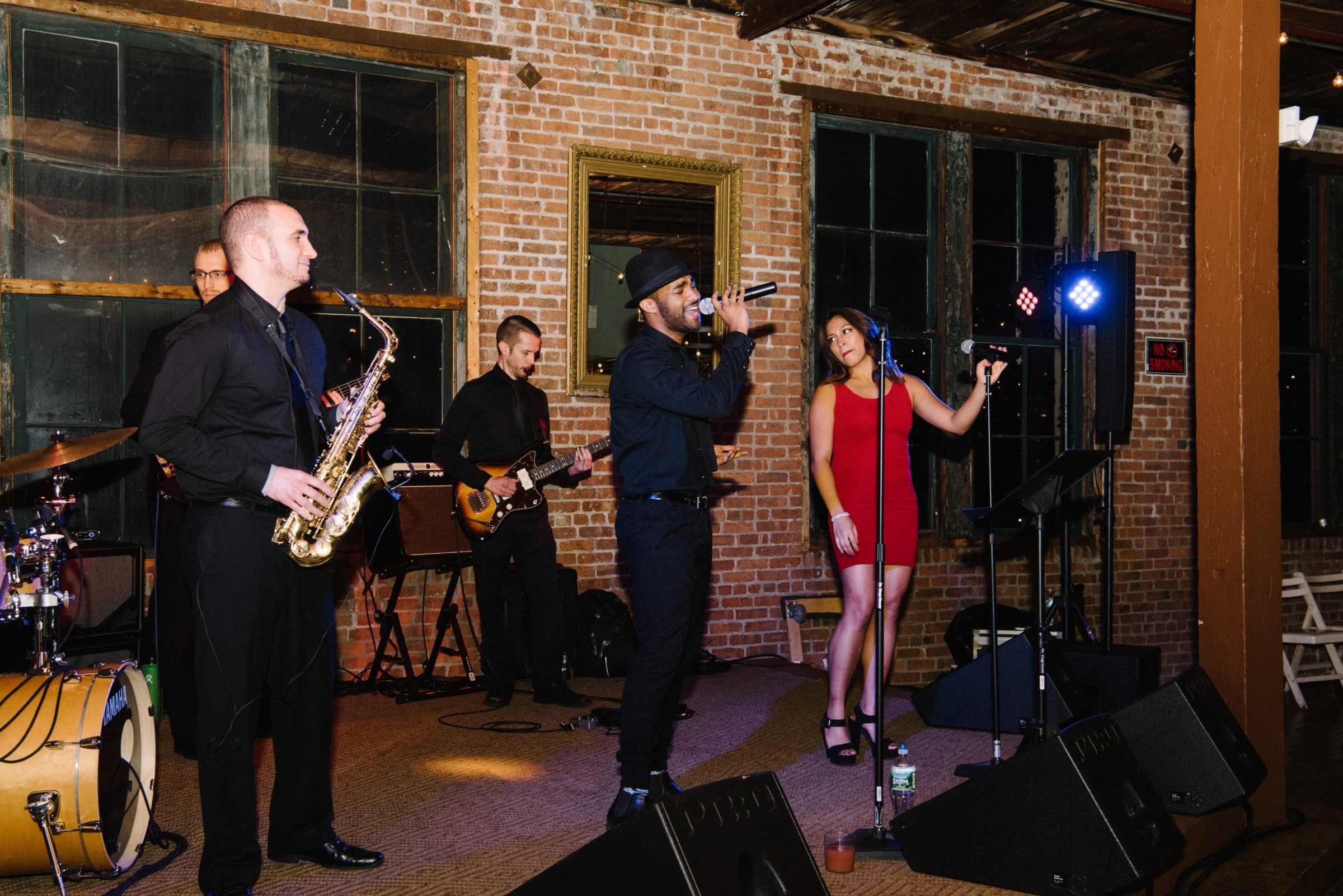 Live band performing in a rustic loft venue with brick walls and a singer in a red dress.