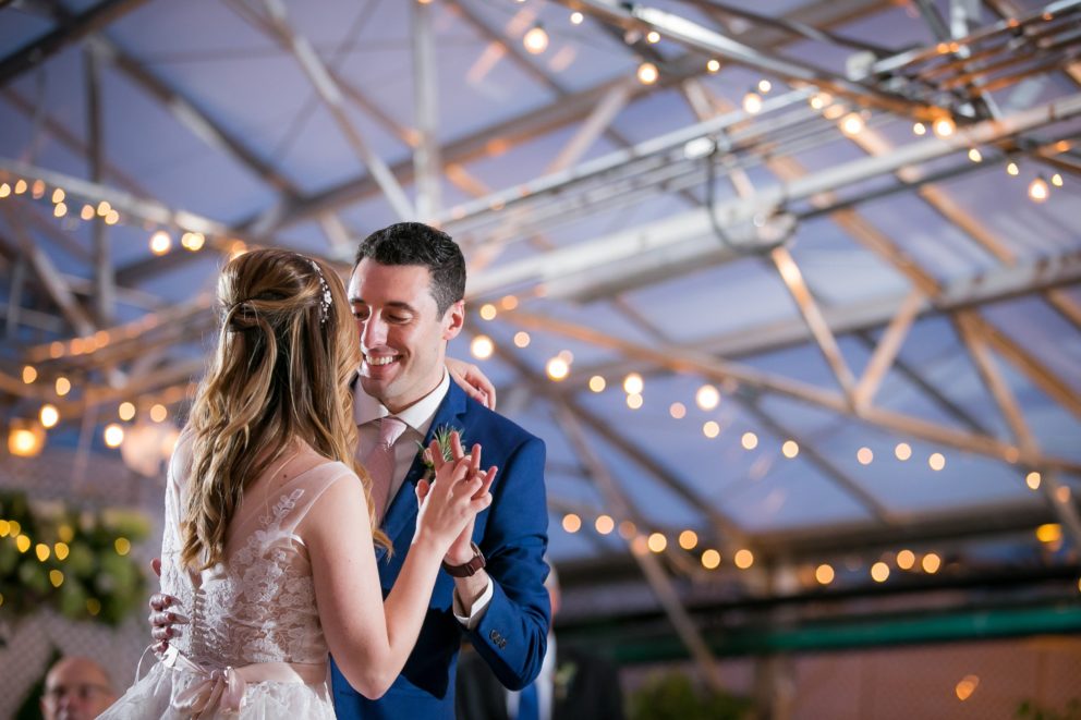 Bride and groom share a romantic first dance under glowing string lights in Philadelphia greenhouse.