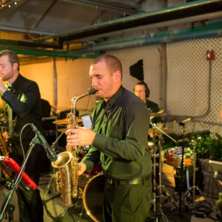 Live jazz band performing with saxophonists, drummer, and vocalist at a Philadelphia indoor venue.